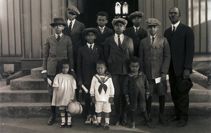 Historic photo of a group of African American youth with older man standing in front of a building.