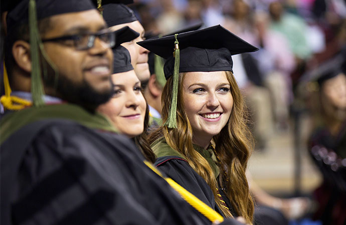 Students sitting in a row at commencement wearing graduation robes and caps.