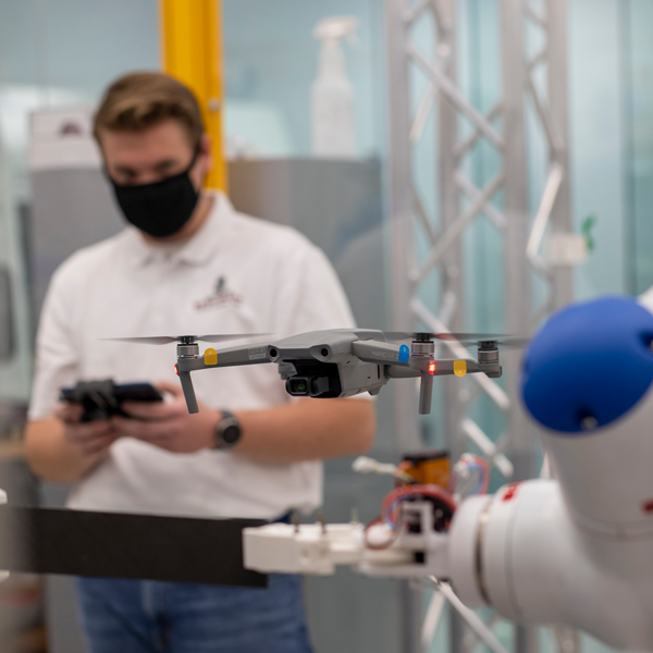 A drone in flight with an engineering student in the background with the controls. 