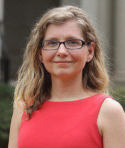 a woman in a sleveless pink dress with dirty blonde shoulder length and rectangular black glasseshair smiling 
