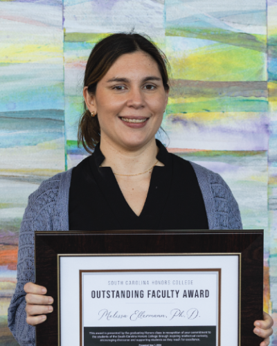 Melissa Ellermann standing in the Koger Center lobby holding her 2025 SCHC outstanding faculty award