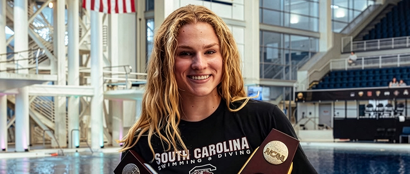 Smiling University of South Carolina diver Sophie Verzyl holding NCAA championship trophy inside aquatic center