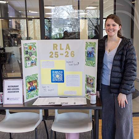 A member of the Restaurant & Lodging Association poses for a photo a student organization fair