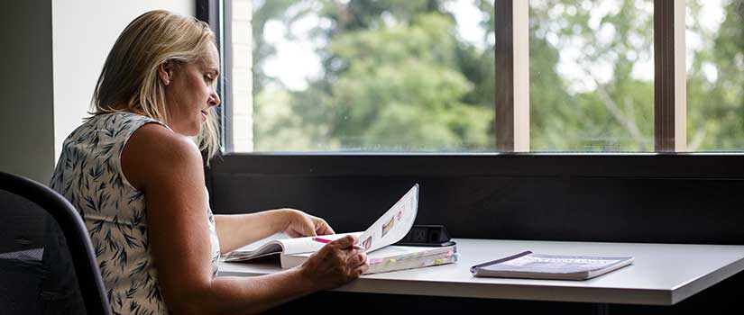 A single student studies in a room with a large window.