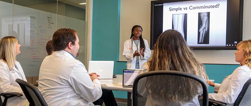 Black female faculty member explains fractures to students in a conference room.