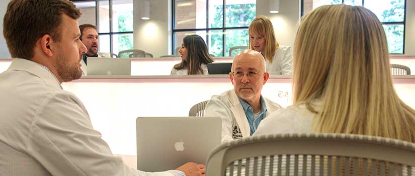 Male and female med students talk with professor in lecture hall