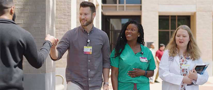 Male med student walks with two female students and fist bumps with a passing friend.