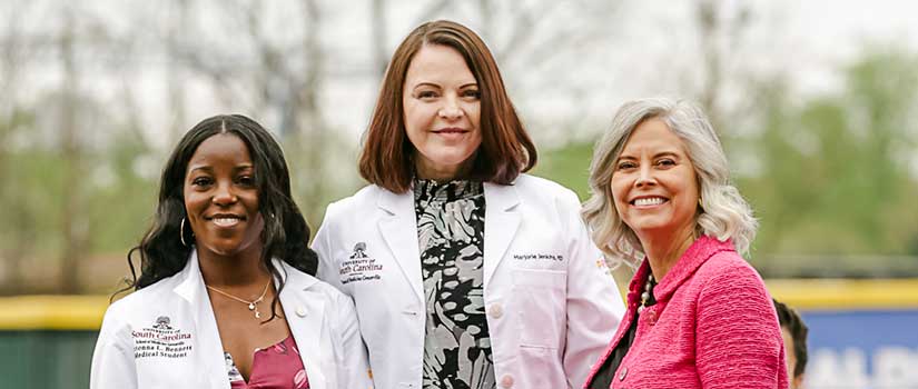 A medical student, the dean and a donor stand together and smile at the camera