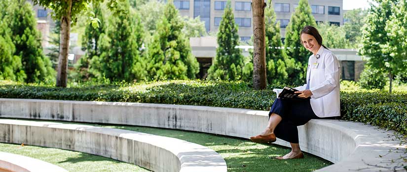 Female medical student with book sitting in outdoor garden area.