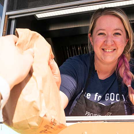 Woman hands food bag to person through serving window.