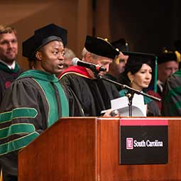 Speaker in academic reaglia at podium during commencement.