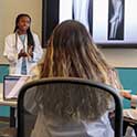 Doctor in white coat speaks in front of class.