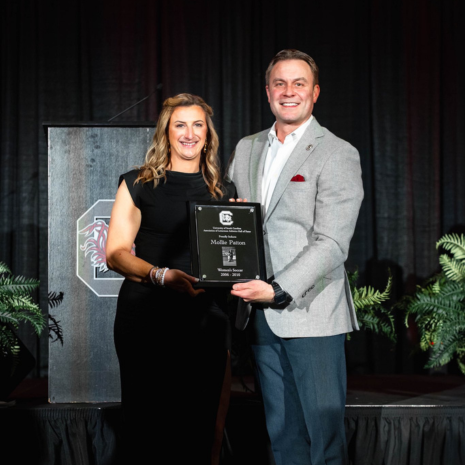 Patton and athletics representative holding plaque on stage