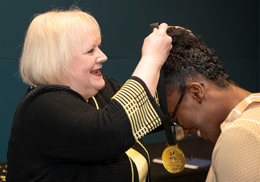 Ann Vail, dean of The Graduate School, puts an award around the neck of an award winner at the 2025 Recognition of Excellence Ceremony