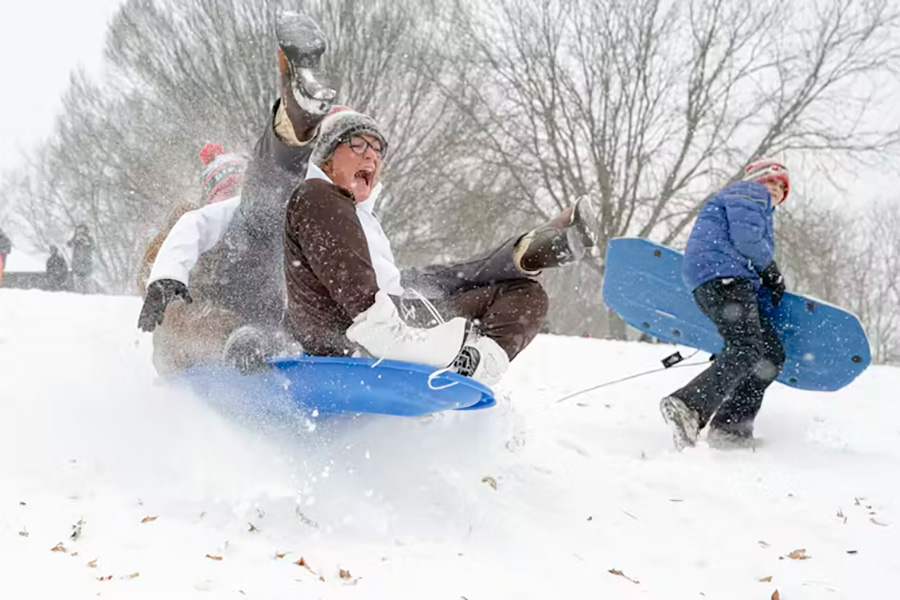 Children are seen using blue plastic sleds to speed down a hillside. 