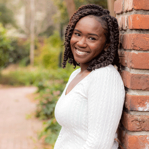 Taylor Jennings-Brown wearing a white sweater leans against brick gate on University of South Carolina's Horseshoe.