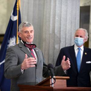 President Bob Caslen gestures above a podium while Governor Henry McMaster observes in the background