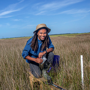 Kamari Boyd kneels on a boardwalk in the marsh