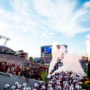 Gamecock football team running out of gate with fans cheering in the stadium.