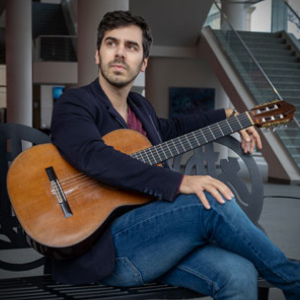 Mak Grgic seated and posed with his guitar in the Koger Center lobby.