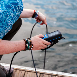 a person kneeling on a dock uses a meter to test water