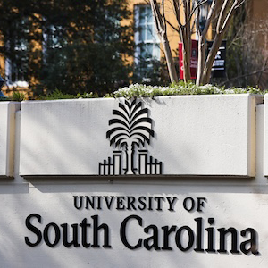 Entrance sign reading University of South Carolina with palmetto tree logo set against landscaped campus background 