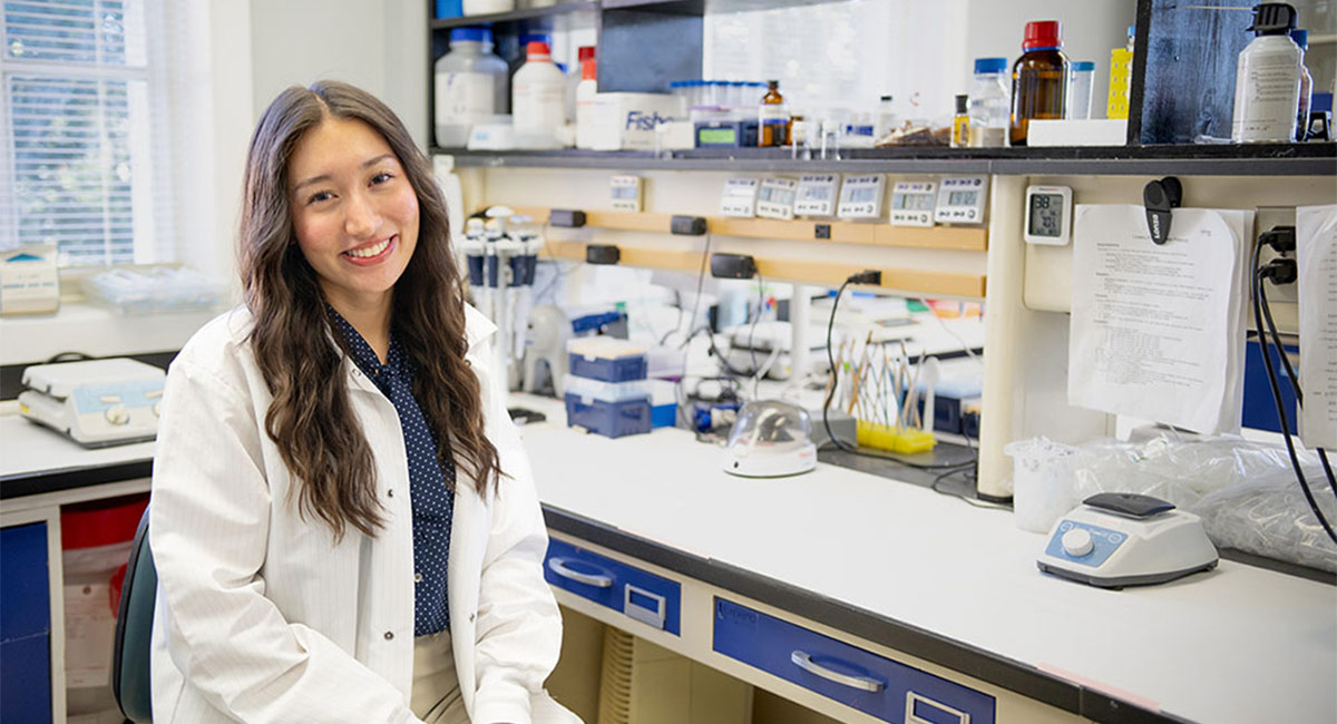 Hannah Brennen sits in white lab coat in lab